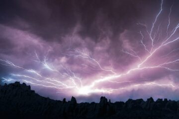 Lightning over a mountain range, against a purple sky